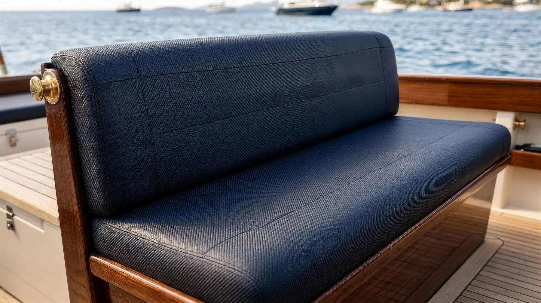 Divanetto di bordo rivestito in Tessuto Morbido blu scuro, con struttura in mogano, borchia in ottone e teak, il mare sullo sfondo
