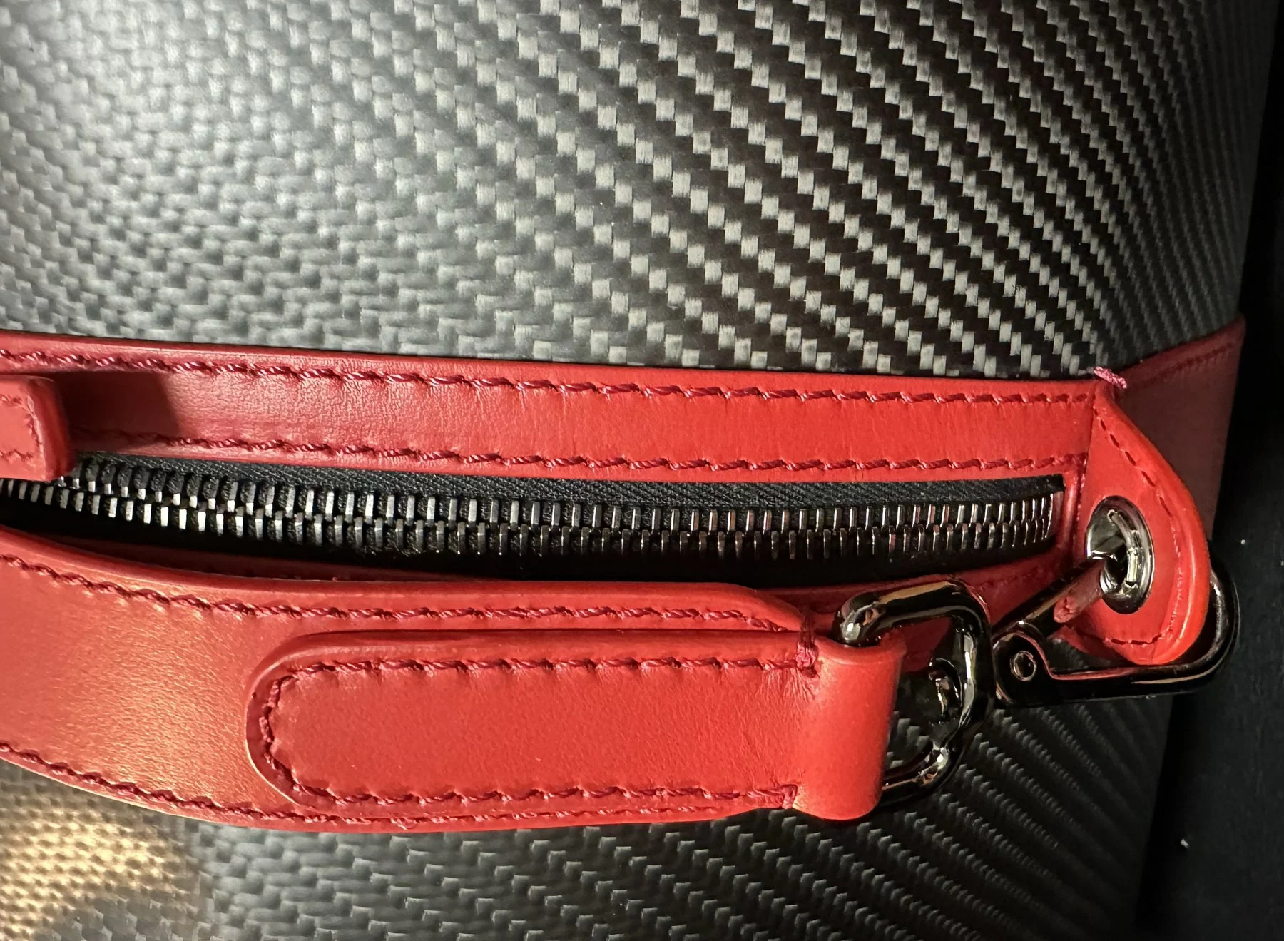 Dettaglio di una borsa in Tessuto Morbido di carbonio con manico e finiture in pelle rossa, zip e gancio metallico